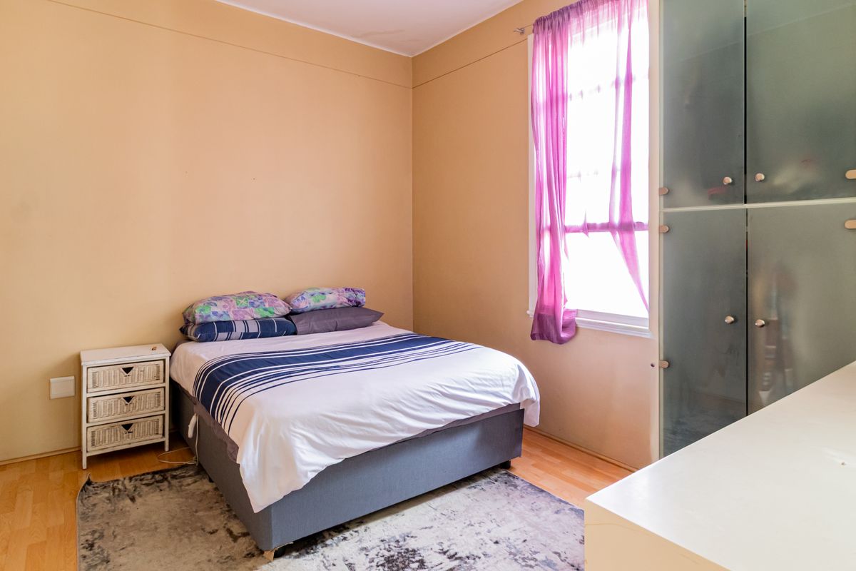 A bedroom featuring laminate flooring, a large window with natural light, and a built-in wardrobe with frosted glass panels.