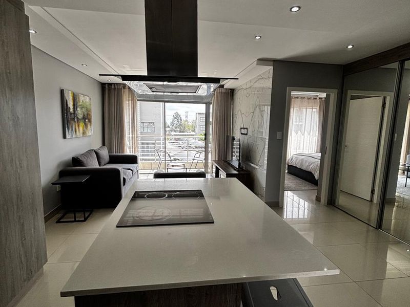 Modern open-plan living area featuring a central kitchen island with integrated hob, sleek cabinetry, tiled floors, and seamless access to a private balcony.