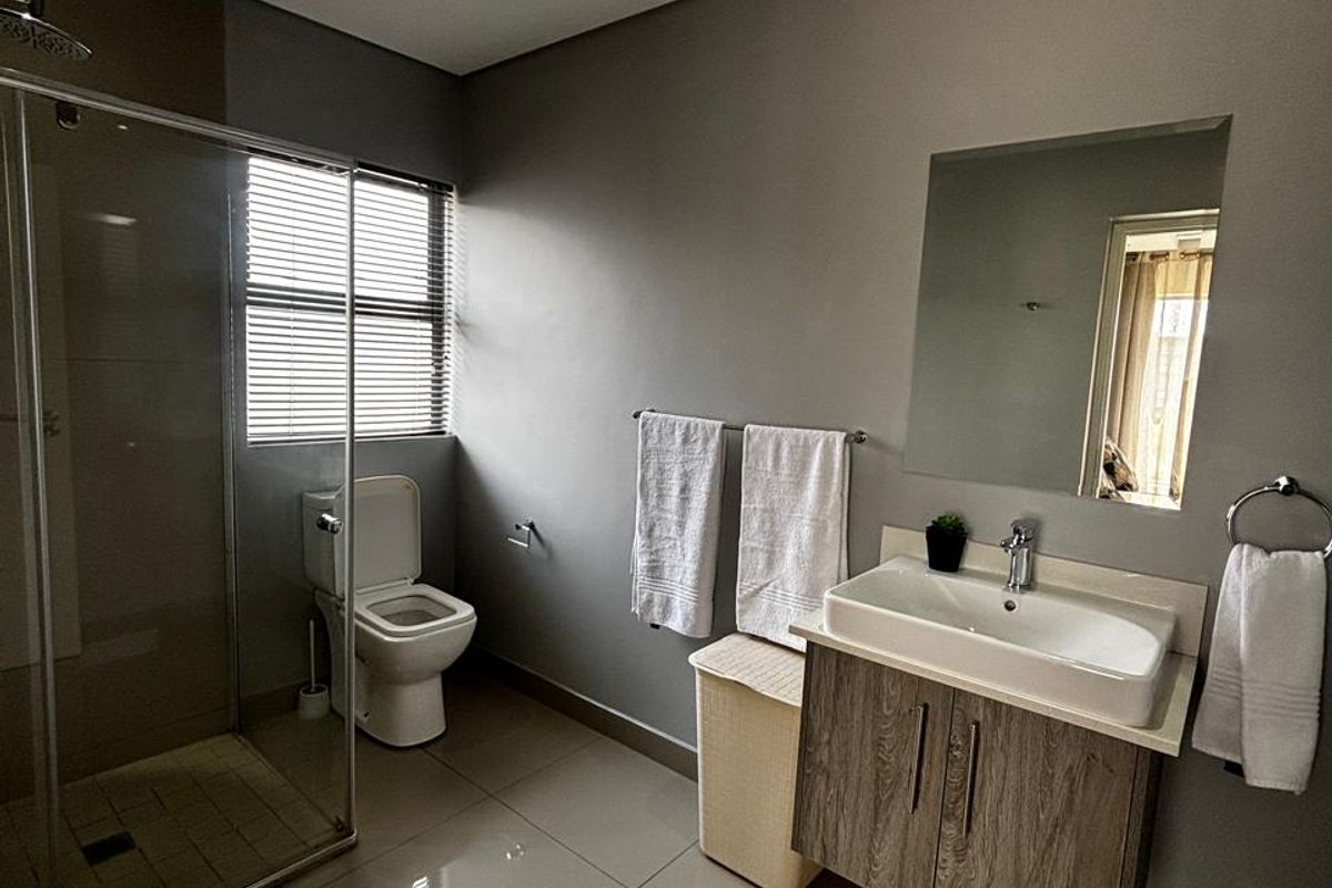 Modern bathroom featuring a glass shower enclosure, wall-mounted vanity with basin, tiled flooring, and neutral grey walls with recessed lighting.