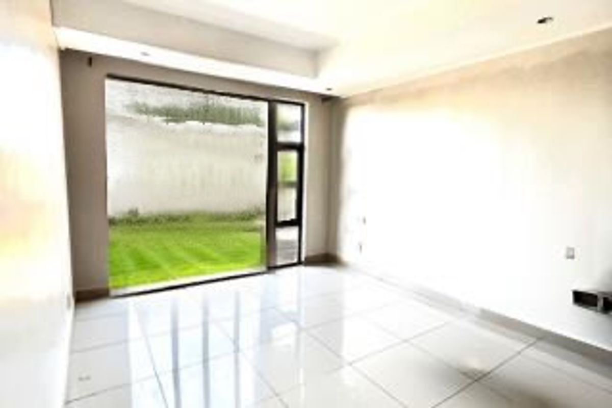 A bright, empty living room featuring large glass sliding doors that open onto a private garden area, finished with polished floor tiles.