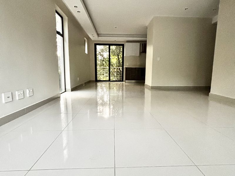 A bright, open-plan living area featuring polished porcelain floor tiles, recessed ceiling lighting, and large glass sliding doors leading to an outdoor balcony.