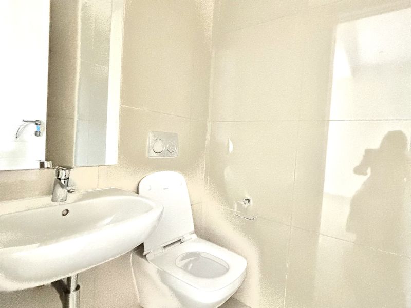 Modern bathroom featuring a wall-mounted toilet, sleek basin with chrome faucet, and large format neutral wall tiles.