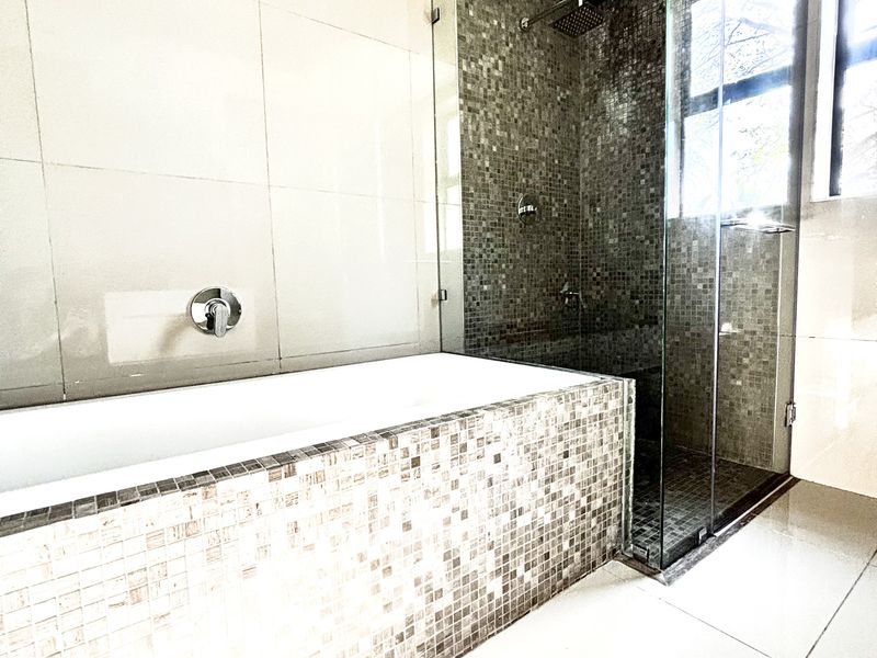 Modern bathroom featuring a tiled bathtub, a separate glass-enclosed shower with mosaic wall detailing, and large format floor tiles.