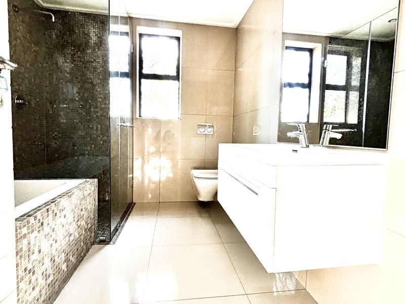 Modern bathroom featuring a floating vanity, large wall-mounted mirror, glass-enclosed shower, and a tiled bathtub with mosaic accents.