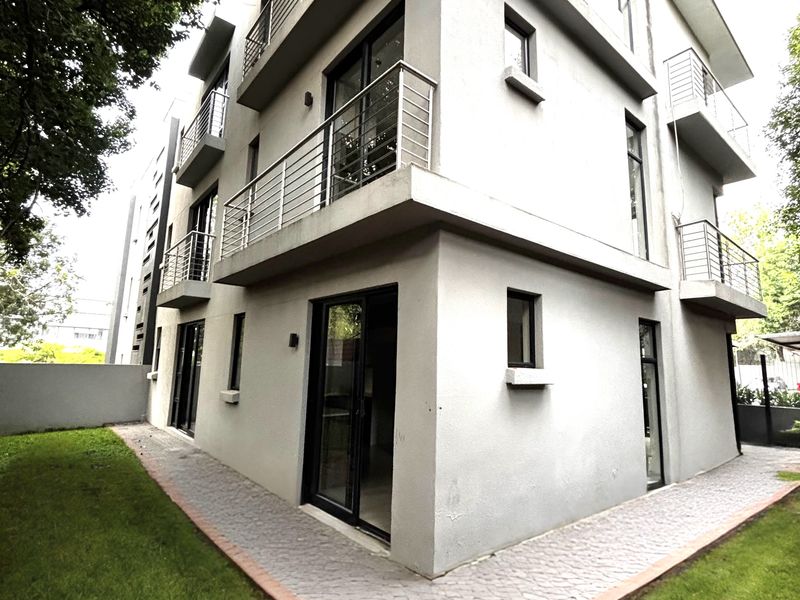 Modern multi-story apartment building exterior featuring stacked balconies with stainless steel railings, paved walkways, and surrounding landscaped garden areas.