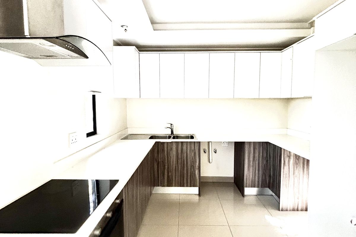 Modern kitchen featuring sleek two-tone cabinetry, integrated electric hob, stainless steel extractor fan, and tiled flooring in a clean, minimalist layout.