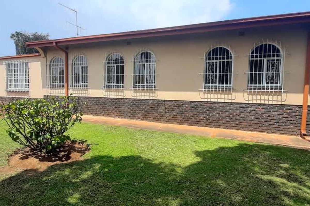 Rear view of the house featuring a brick base, rendered walls, arched windows with security bars, and a well-maintained lawn.