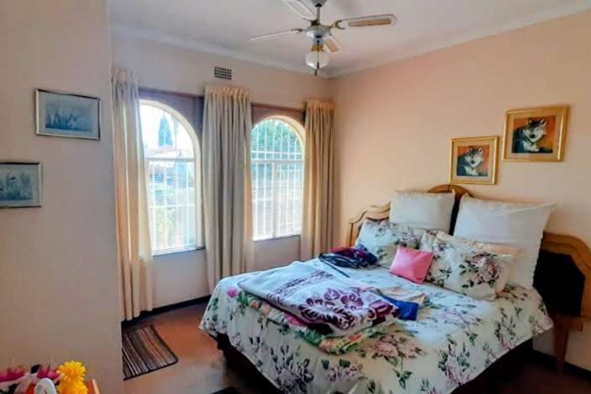A bedroom featuring arched windows with security bars and a ceiling fan, providing natural light and ventilation.