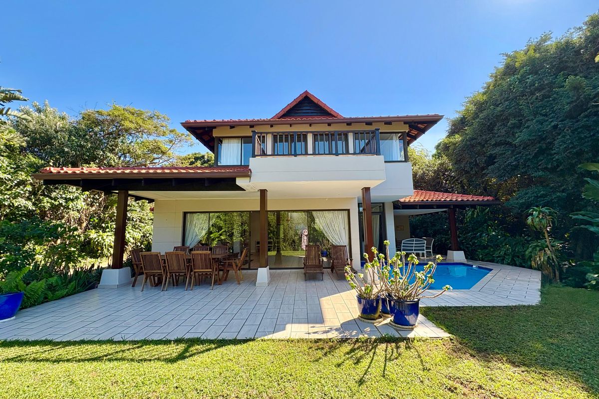 A spacious rear exterior view featuring a covered patio, tiled flooring, a swimming pool, and a two-story house with a balcony.