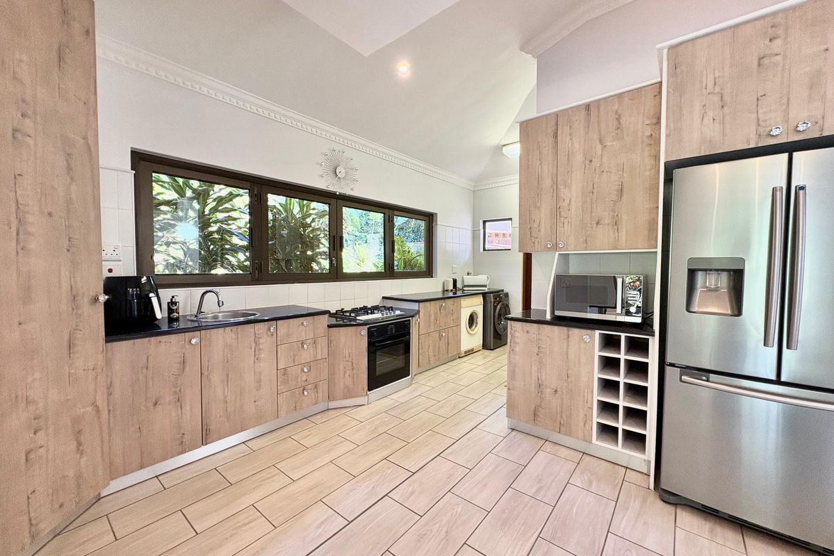 Modern kitchen featuring wood-look cabinetry, dark countertops, integrated oven and hob, and tiled flooring with ample natural light.