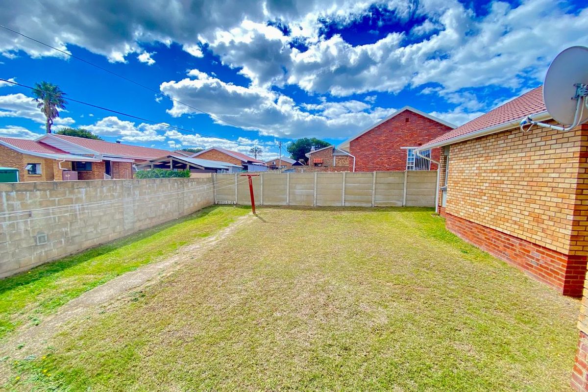 A private rear garden featuring a lawn area, enclosed by precast concrete boundary walls, adjacent to the brick-built main dwelling.