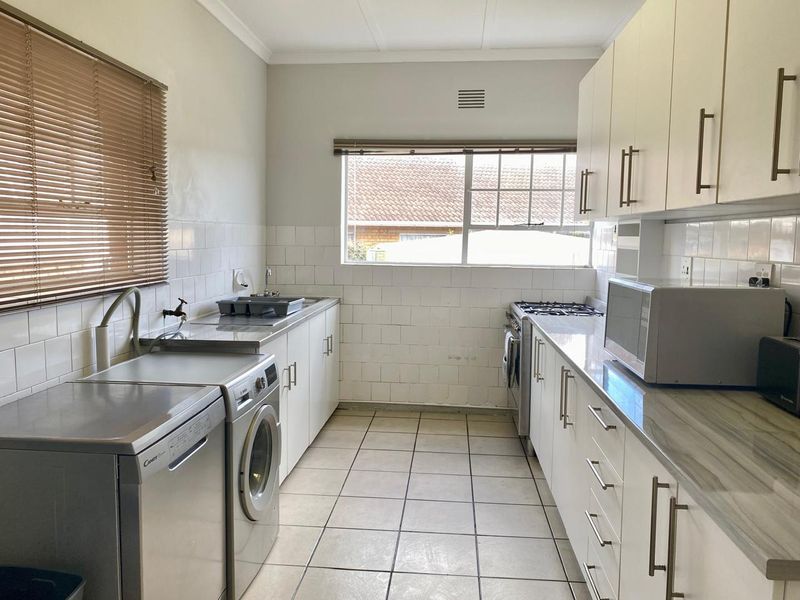 Functional kitchen featuring white cabinetry, tiled splashbacks, gas hob, oven, and integrated laundry space with tiled flooring.