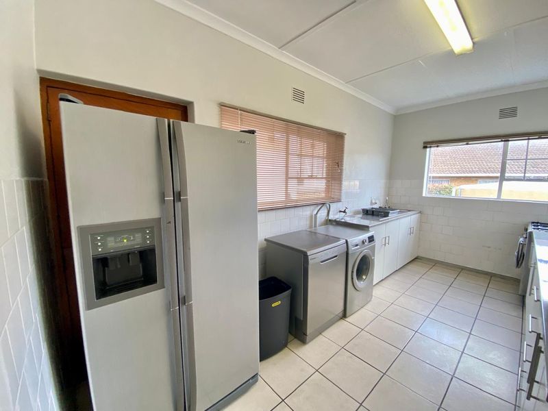 A functional scullery area featuring tiled flooring, built-in cabinetry, a stainless steel sink, and tiled splashbacks, providing practical utility space.