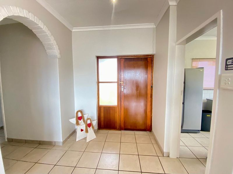 A bright entrance hall featuring tiled flooring, a decorative brick archway, and a traditional timber front door leading into the home.