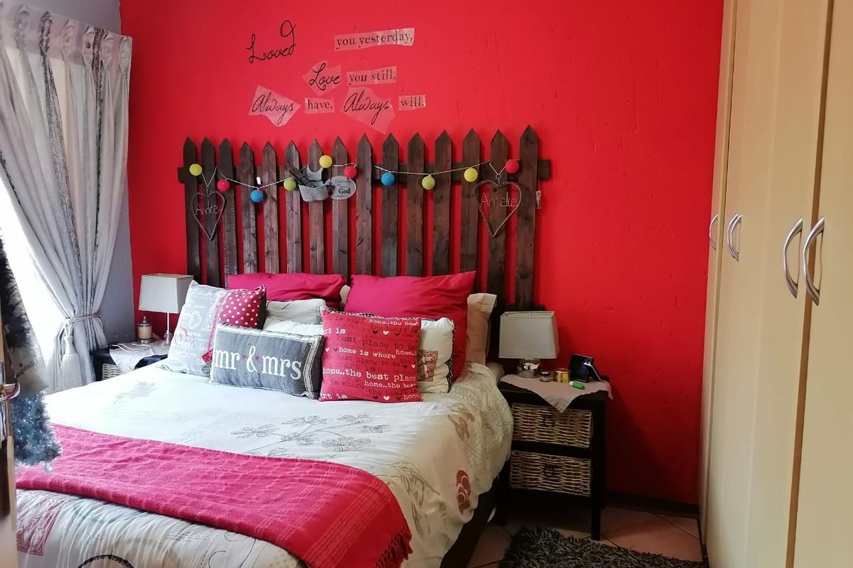 A bedroom featuring built-in cupboards and tiled flooring, currently styled with a bold red accent wall.