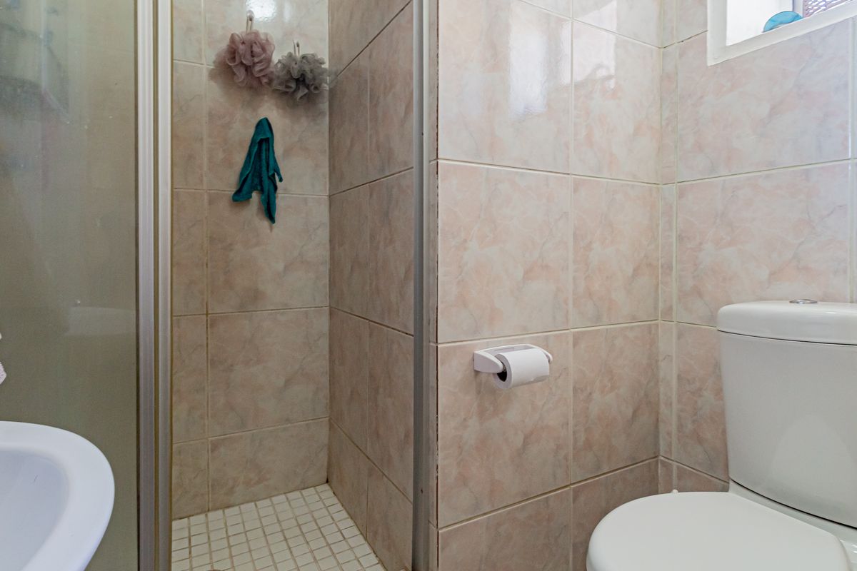 A compact bathroom featuring a shower enclosure with tiled walls, a standard toilet, and a small basin.