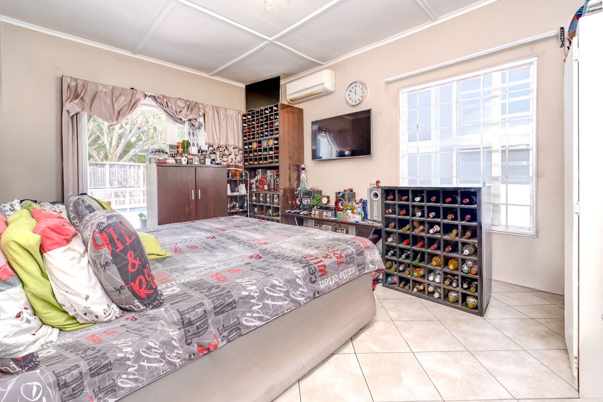 A bedroom featuring tiled flooring, a wall-mounted air conditioning unit, and security bars on the windows, with direct access to an outdoor area.