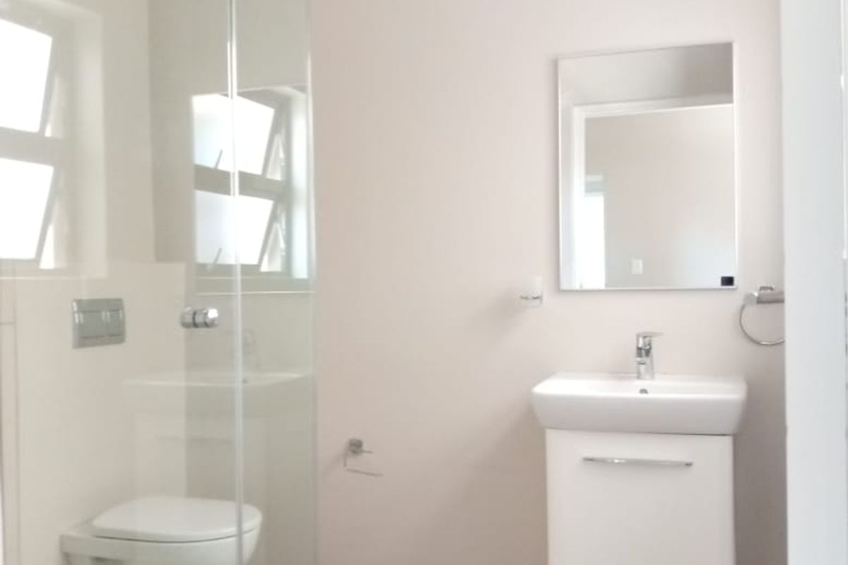 A modern, clean bathroom featuring a wall-mounted toilet, a glass-enclosed shower, and a contemporary vanity with a basin and mirror.