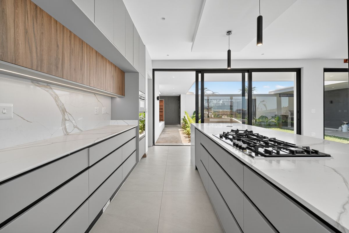 Modern, high-end kitchen featuring sleek grey cabinetry, marble-look stone countertops, a central island with a gas cooktop, and seamless access to the outdoor patio.