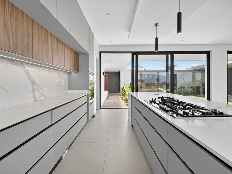 Modern, high-end kitchen featuring sleek grey cabinetry, marble-look stone countertops, a central island with a gas cooktop, and seamless access to the outdoor patio.