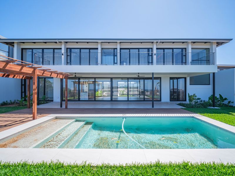 Rear elevation of a modern two-story house featuring a swimming pool, wooden deck, pergola, and expansive glass sliding doors leading to the interior.