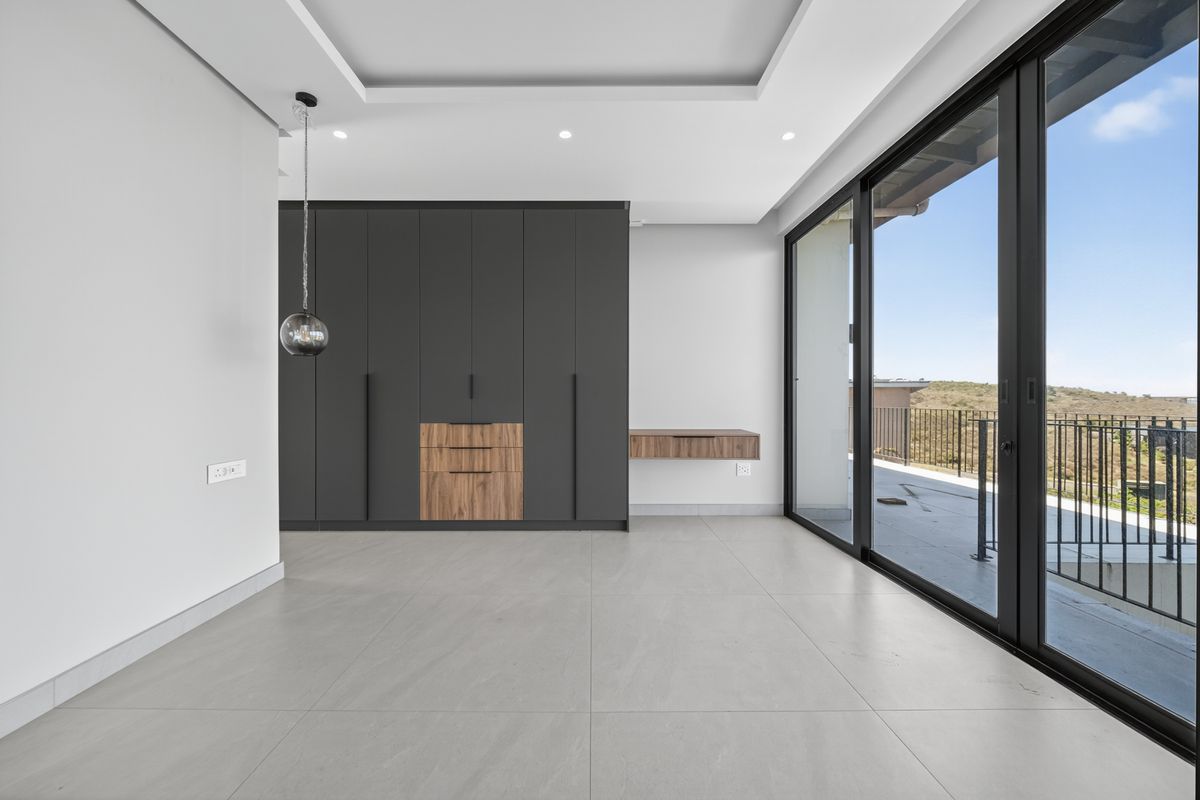 Modern bedroom featuring sleek dark built-in cupboards, a floating vanity, large sliding glass doors leading to a balcony, and neutral tiled flooring.
