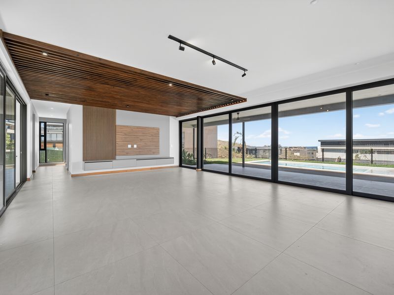 Spacious open-plan living area featuring a striking timber slat ceiling, built-in media cabinetry, and large sliding doors opening to the pool and garden.