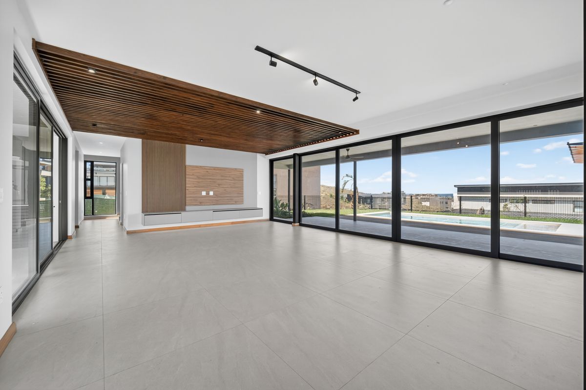 Spacious open-plan living area featuring a striking timber slat ceiling, built-in media cabinetry, and large sliding doors opening to the pool and garden.