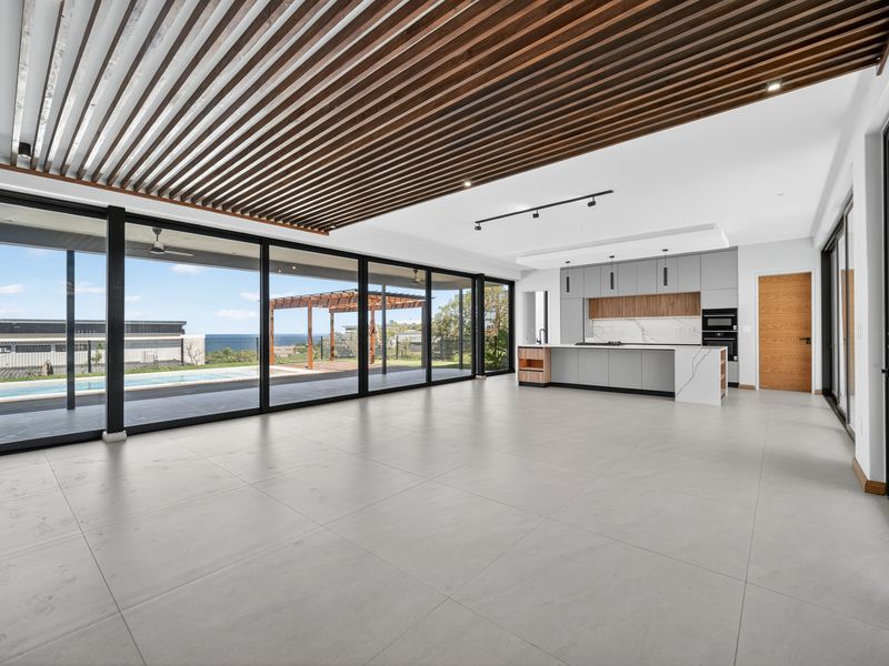 Spacious open-plan living and kitchen area featuring a striking slatted timber ceiling, large format tiles, and expansive glass doors opening to the pool area.