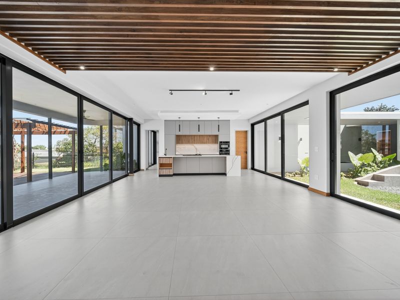 Spacious open-plan living area featuring a modern kitchen, slatted timber ceiling, and expansive sliding glass doors opening to the garden and patio.