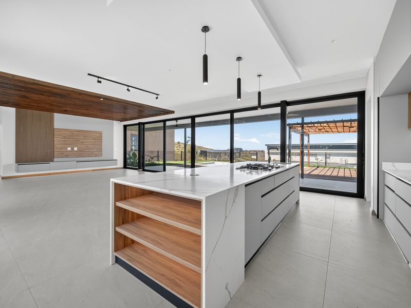 Modern open-plan living and kitchen area featuring a large stone-topped island, sleek cabinetry, timber ceiling accents, and expansive sliding doors leading to the patio.