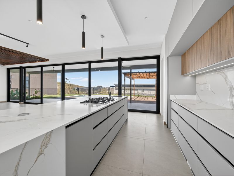 Modern open-plan kitchen featuring a large marble-look island with gas cooktop, sleek cabinetry, and expansive sliding doors opening to the outdoor patio area.