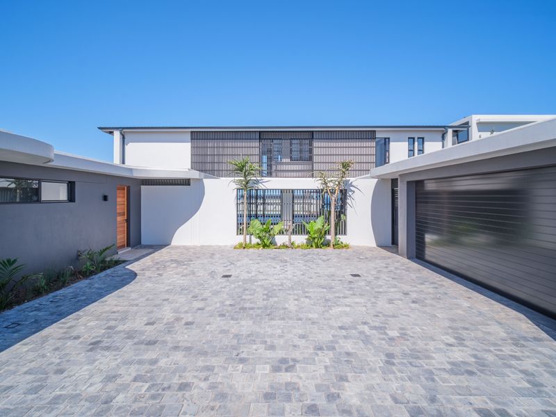 Modern front facade featuring a paved driveway, integrated garage, timber entrance door, and contemporary architectural detailing with clean lines and neutral finishes.