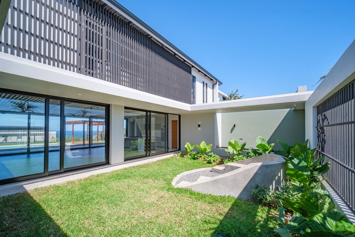 A modern rear courtyard featuring a landscaped garden, concrete planter, and large sliding glass doors connecting to the interior living spaces.