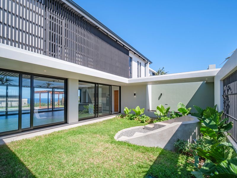 A modern rear courtyard featuring a landscaped garden, concrete planter, and large sliding glass doors connecting to the interior living spaces.
