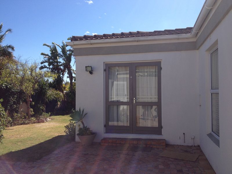 Rear exterior view of the property featuring a brick paved patio area, double glass doors, and well-maintained garden surroundings.