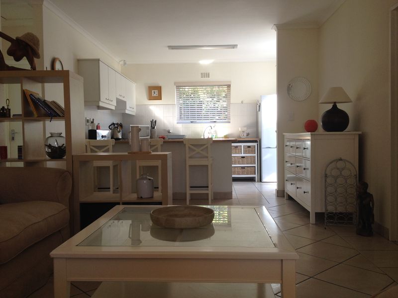An open-plan living and kitchen area featuring tiled flooring, white cabinetry, and a functional kitchen layout with a breakfast bar.