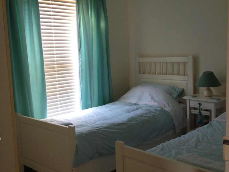 A functional bedroom featuring neutral walls, light flooring, and window treatments including venetian blinds and curtains.
