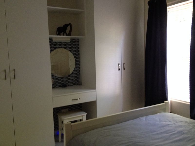 A bedroom featuring white built-in cupboards and a matching integrated vanity unit with shelving.