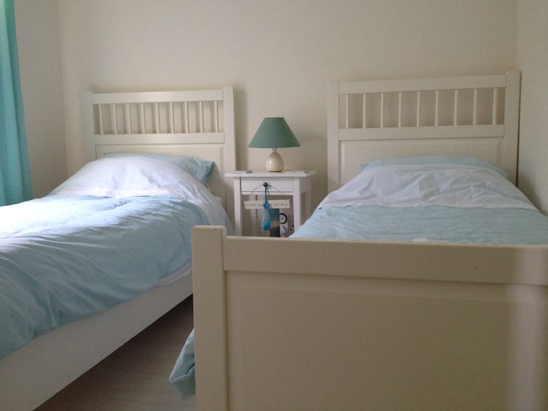 A bedroom featuring two single beds with a central bedside table, finished with neutral wall tones.