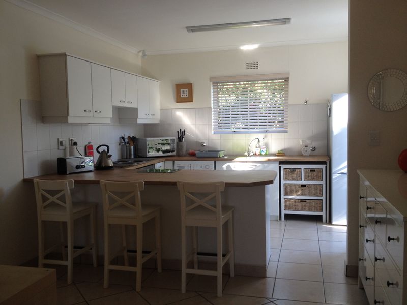 A functional kitchen featuring white cabinetry, a wooden breakfast bar, tiled splashbacks, and tiled flooring, offering a practical layout for daily use.