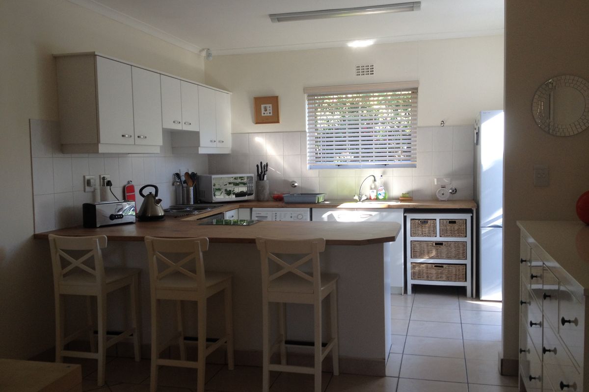 A functional kitchen featuring white cabinetry, a wooden breakfast bar, tiled splashbacks, and tiled flooring, offering a practical layout for daily use.