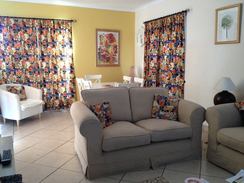 A living room area featuring tiled flooring and large windows with patterned curtains, providing a functional and lived-in space.