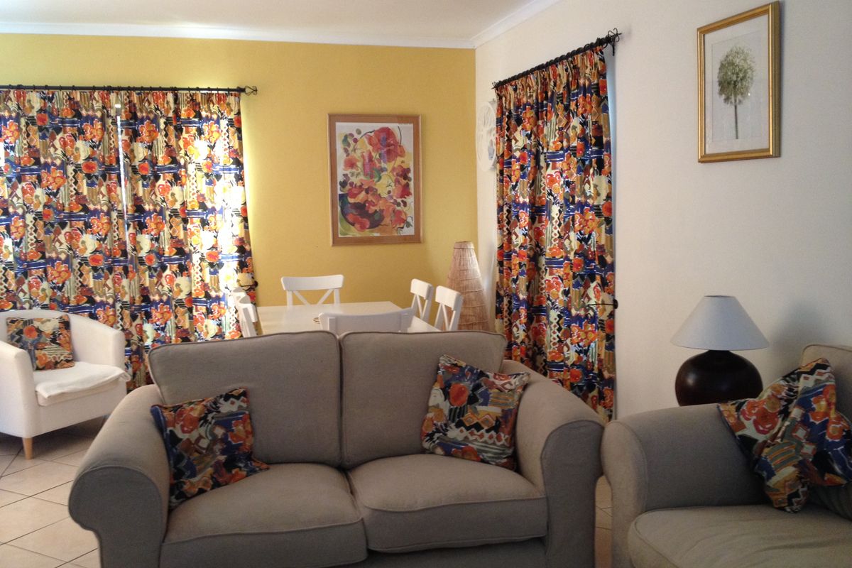 A living and dining area featuring tiled flooring and large windows with curtain rods, offering a functional space with potential for modern updates.