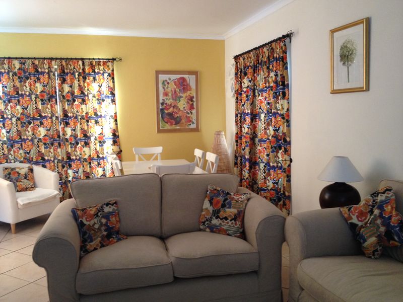 A living and dining area featuring tiled flooring and large windows with curtain rods, offering a functional space with potential for modern updates.