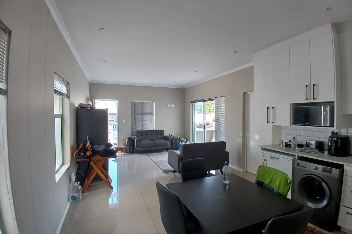 Open-plan living area featuring tiled floors, modern white kitchen cabinetry with integrated appliances, and sliding door access to the exterior.