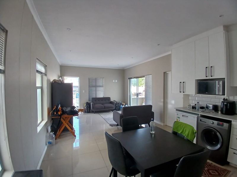Open-plan living area featuring tiled floors, modern white kitchen cabinetry with integrated appliances, and sliding door access to the exterior.