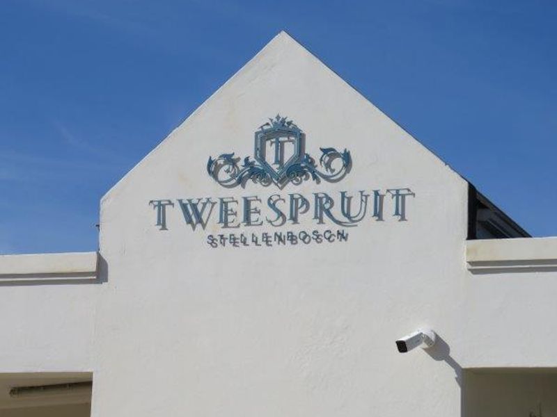 The front entrance facade of the Tweespruit estate in Stellenbosch, featuring prominent building signage and a mounted security camera.