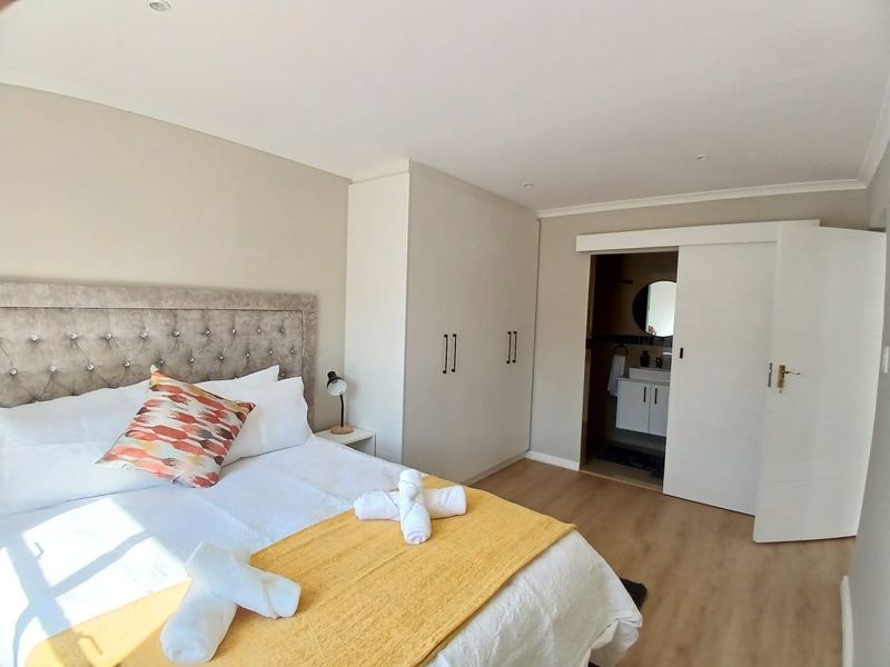 A well-maintained bedroom featuring laminate flooring, built-in cupboards, and an en-suite bathroom accessed via a sliding door.