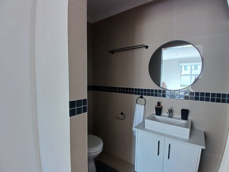 A modern bathroom featuring a white vanity cabinet with a vessel sink, neutral wall tiles with a decorative border, and a circular mirror.